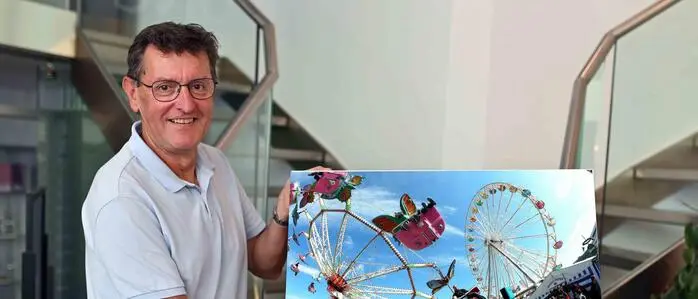 Ein Mann hält ein Bild in der Hand. Darauf zu sehen ist der St. Veiter Wiesenmarkt.