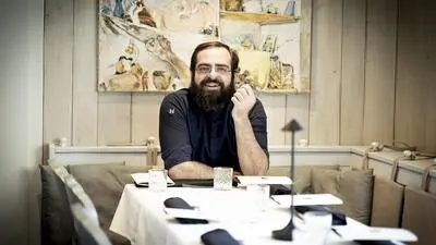 Der Koch sitzt im Foto am gedeckten Tisch und lacht in die Kamera