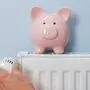 Close-up Of Man's Hand Adjusting Thermostat With Piggy Bank On Radiator