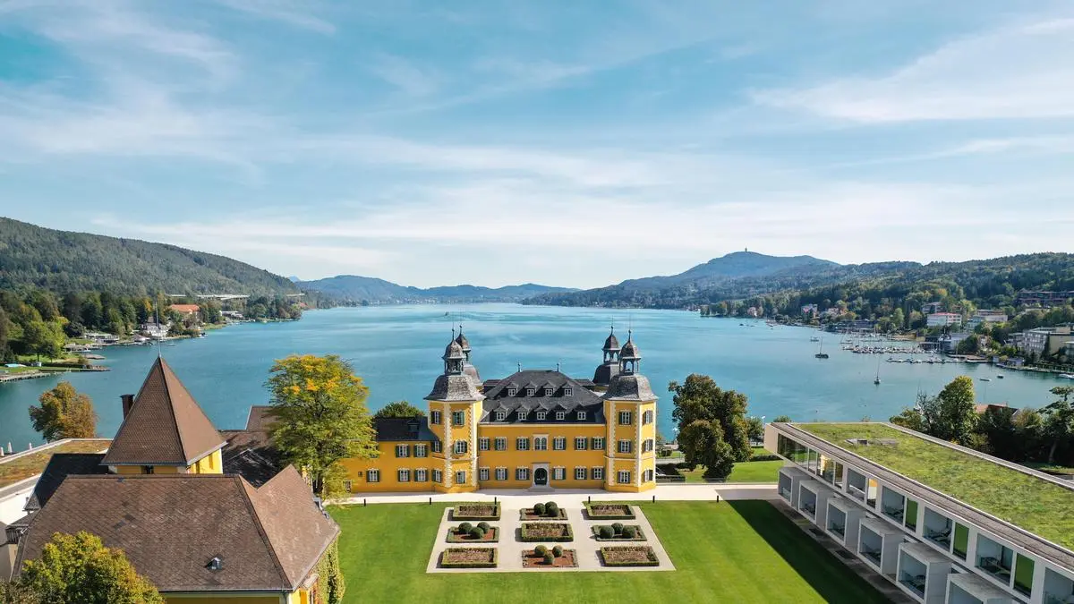 Man sieht das Schlosshotel Velden von hoher Höhe aus in Richtung Wörthersee fotografiert, davor die schöne Wiese | Schlosshotel Velden