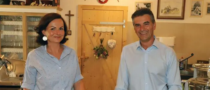 Ein Mann und eine Frau, beide tragen blaue Oberteile, stehen in einem hölzernen Haus.