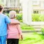 Back view of nurse caregiver support walking with elderly woman outdoor