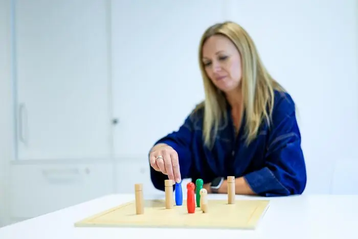 Eine Psychologin sitzt vor einer Holzplatte mit bunten Figuren darauf.