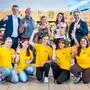 Jugendliche in gelben Shirts und mehrere Erwachsene posieren in einem Lebensmittelgeschäft