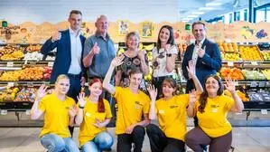 Jugendliche in gelben Shirts und mehrere Erwachsene posieren in einem Lebensmittelgeschäft