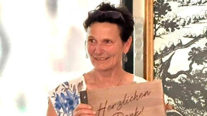 Eine Dame mit kurzen schwarzen Haaren hält ein Schild mit der Aufschrift „Herzlichen Dank“ in Händen