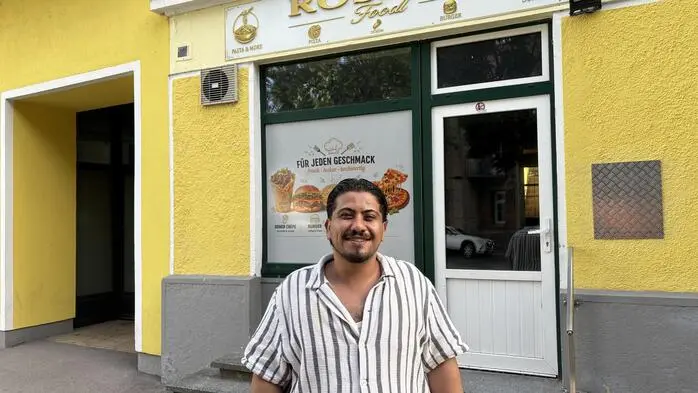 Ein Mann im kurzärmligen Hemd vor einem Fast-Food-Lokal mit der Aufschrift „Rosana“