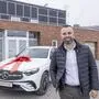 Ein Mercedes-SUV mit großer roter Schleife vor einem Backsteingebäude, daneben ein Mann mit kurzem Bart, weißem Hemd und schwarzer Jacke | Der Autoverkäufer Andreas Blazevic eröffnet in Villach einen Gebrauchtwagenhandel