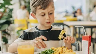 Ein Bub sitzt am Tisch und isst Pommes und trinkt Saft