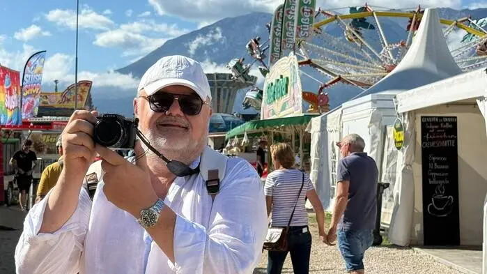 Ein Mann mit weißem Hemd, Brille und Kappe hält eine Kamera hoch, im Hintergrund das Marktgelände