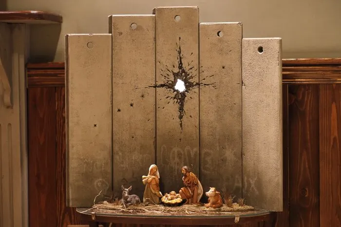 Die Krippe des Street-Art-Künstlers Banksy steht vor einer Wand mit Detonationsloch.