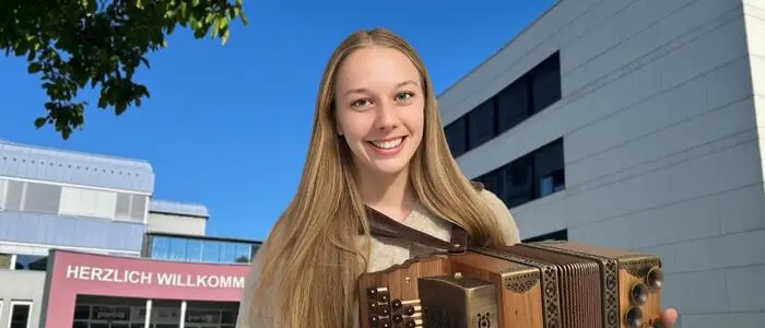 Eine Musikerin mit Harmonika vor einem Schulgebäude