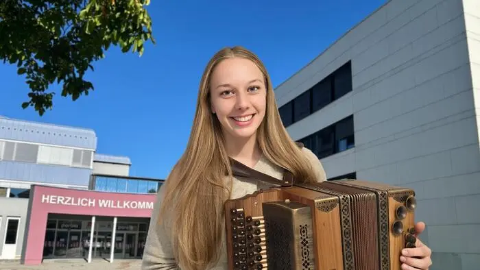 Eine Musikerin mit Harmonika vor einem Schulgebäude