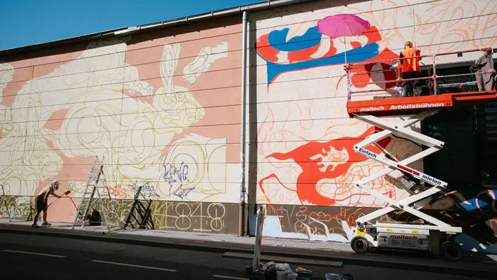 Malerinnen und Maler gestalten eine riesige Wand mit bunten Bildern.
