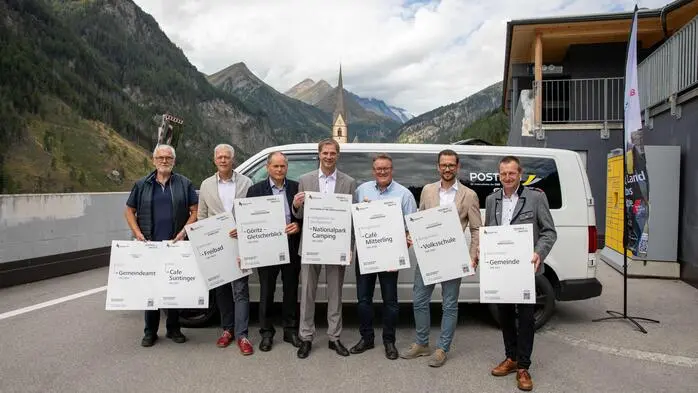 Sieben Männer vor einem Kleinbus und lachen in die Kamera
