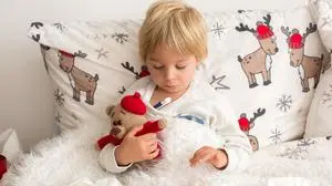 Beautiful blond toddler child, sick boy with fever, lying in bed on Christmas, coughing and having running nose