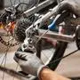 Cropped shot of male mechanic working in bicycle repair shop, mechanic repairing bike using special tool, wearing protective gloves