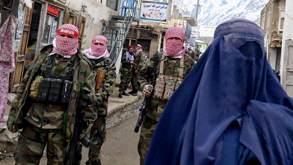 Taliban-Kämpfer stehen hinter einer Frau mit Burka | Seit 2021 wird Afghanistan wieder von den radikalen Taliban beherrscht.