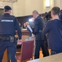Das Foto zeigt den Angeklagten im Gerichtssaal umgeben von Polizisten
