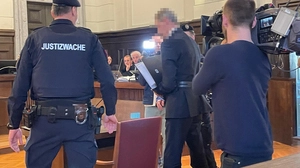 Das Foto zeigt den Angeklagten im Gerichtssaal umgeben von Polizisten