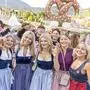 Fünf junge Frauen im Dirndl lachen in die Kamera, hinter ihnen ist ein Vergnügungspark