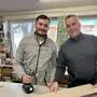 Zwei Männer stehen in einer Werkstatt und halten ein Brett und einen Bohrer