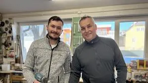 Zwei Männer stehen in einer Werkstatt und halten ein Brett und einen Bohrer