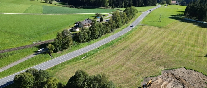 Zu sehen ist eine Straße, die sich durch Wiesen schlängelt