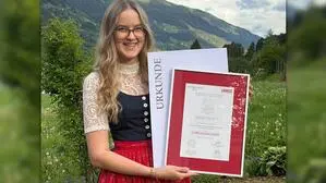 Eine junge Frau in Tracht steht auf einer Wiese und hält eine Urkunde in die Kamera