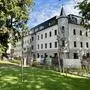 Blick von einer Wiese zu einem historischen Gebäude mit frisch renovierter Fassade. Vor dem Haus sind noch Reste einer Baustelle zu sehen