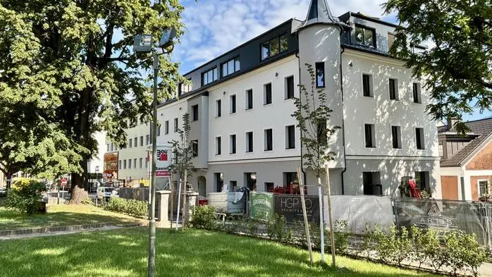 Blick von einer Wiese zu einem historischen Gebäude mit frisch renovierter Fassade. Vor dem Haus sind noch Reste einer Baustelle zu sehen