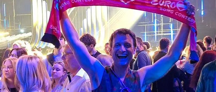 Ein Mann in Tracht steht in einer Halle voller Menschen und hält einen Fanschal in die Kamera