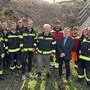 Eine Gruppe von Männern in Feuerwehruniform steht vor einem Stromkasten und lächelt in die Kamera.