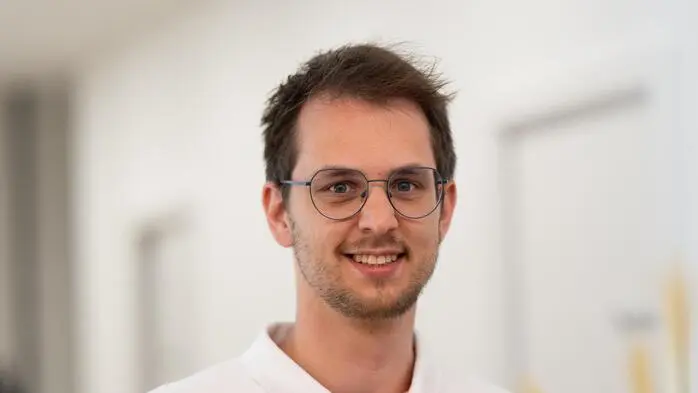 Ein Mann mit Brille und weißem Poloshirt lächelt in die Kamera