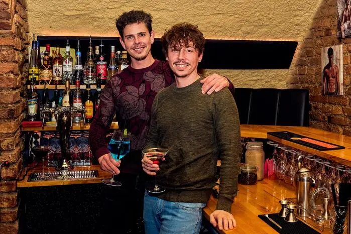 Strass Underground Bar:
Seit Oktober 2025 betreiben Emanuel und René Kolmanz in der Purtscherstraße in Klagenfurt die „Strass Underground Bar“. Innerhalb weniger Monate hat das Paar im Kellerlokal einen neuen Treffpunkt für die LGBTQI-Community und alle geschaffen, die queeres Flair schätzen.
Emanuel Kolmanz bringt als Absolvent der Hotelfachschule Bad Gleichenberg Erfahrung aus der Gastronomie mit. Persönliche Betreuung steht für ihn im Mittelpunkt. „Wenn ich Gäste so behandle, wie ich gerne behandelt werden möchte, funktioniert das. Die Leute schätzen das“, sagt Kolmanz. Sie hoffen die Community stärker zusammenzubringen und Klagenfurt weiter für queeres Leben zu öffnen. Am Freitag, 28. August, sind sie Gastgeber der Club-Night-Afterparty.
