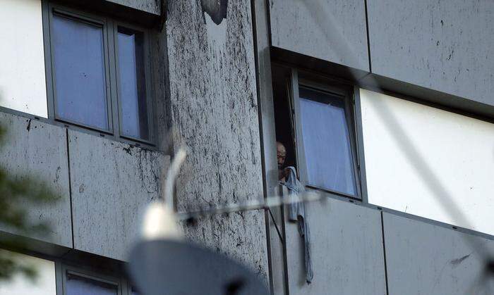 Eine Person blickt aus einem Fenster des brennenden Gebäudes.