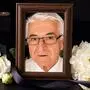 Trauersujet: In einem Bilderrahmen: Porträt eines älteren Mannes mit Brille, weißen Haaren und Hemd. Davor weiße Blumen und eine schwarze Schleife