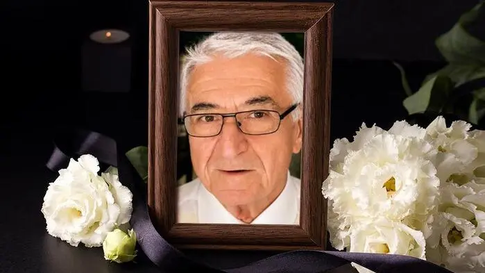 Trauersujet: In einem Bilderrahmen: Porträt eines älteren Mannes mit Brille, weißen Haaren und Hemd. Davor weiße Blumen und eine schwarze Schleife