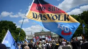 A participant holds a flag in the colors of Germany and the far-right Alternative for Germany (AfD) party, reading "We are the People", during a demonstration titled "Frieden - Freiheit - Volksabstimmung" (Peace - Freedom - Referendum) organised by a network called "Deutschland steht auf" (Germany stands up) including far-right groups and members of the so-called "Querdenker" (lateral thinkers) movement, on May 24, 2025 in Berlin. (Photo by RALF HIRSCHBERGER / AFP)