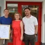 Drei Personen sind auf dem Bild zu sehen: Zwei Männer und eine Dame im roten Kleid 