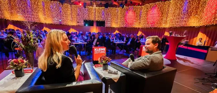 Zwei Menschen sitzen auf einer Bühne, dahinter ist das Publikum zu sehen