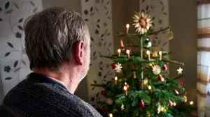 Worms, Rhineland-Palatinate, Germany - December 27, 2024: An elderly man stands alone in front of a decorated Christmas tree, the Christmas festivities in his living room seem quiet and contemplative. Symbolic image Celebrating Christmas alone *** Ein älterer Mann steht alleine vor einem geschmückten Christbaum, das weihnachtliche Fest im Wohnzimmer wirkt still und nachdenklich. Symbolbild Weihnachten alleine feiern