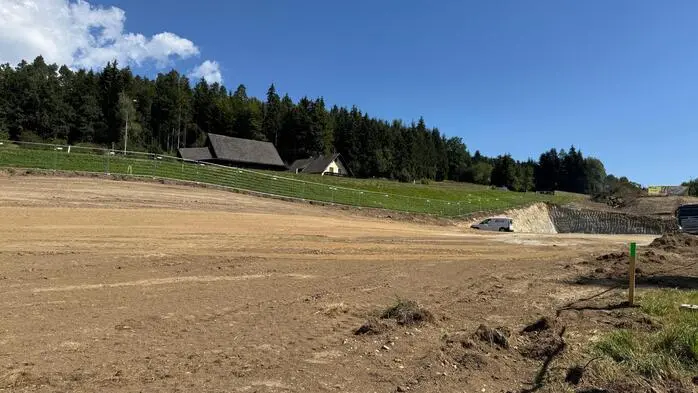 Eine Wiese auf der Erdbewegungen durchgeführt werden. Dahinter sieht man ein Haus und Wald
