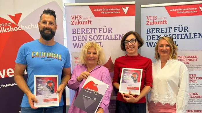 Drei Frauen und ein Mann stehen vor Roll-ups und halten ein Kursprogramm in den Händen