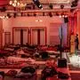 Viele Personen liegen in einem großen Raum am Boden, auf der Bühne Instrumente und Musiker, gedämmtes Licht