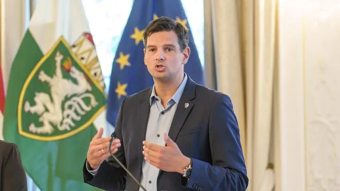 Hannes Amesbauer spricht an einem Rednerpult, dahinter sind die steirische und die EU-Fahne zu sehen