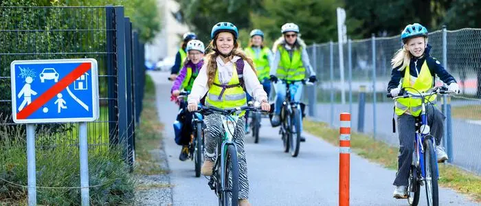 Ein paar Mädchen fahren mit dem Fahrrad. Sie tragen eine Warnweste und einen Helm.