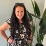 Eine junge Dame mit langen schwarzen Haaren und schwarz-geblümten Kleid blickt in die Kamera