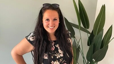 Eine junge Dame mit langen schwarzen Haaren und schwarz-geblümten Kleid blickt in die Kamera