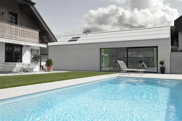 Ein schlanker, längsgestreckter, schlicht ausgeführter Bau mit wenigen, klar definierte Öffnungen, die bewusst Ein- und Ausblicke zulassen. Der Architekt plante ein Haus, das sich als untergeordneter Baukörper am Hauptgebäude orientiert.
